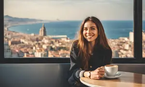 Uśmiechnięta dziewczyna z kawą, jak z hiszpańskie dziewczyny tekst, podziwia panoramę miasta i morza.