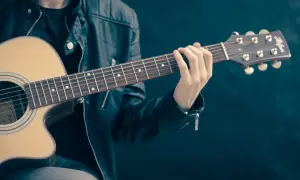 Mężczyzna w skórzanej kurtce uczy się, jak szarpać struny na gitarze. Jego palce zaciskają akord na gryfie.