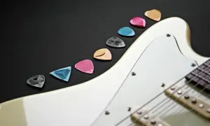 Różnokolorowe kostki do gitary elektrycznej leżą obok białej gitary. Wybierz odpowiednią, by zacząć naukę, jak nastroić gitarę elektryczną.