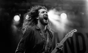 Charyzmatyczny gitarzysta z rozwianymi włosami śpiewa z pasją, grając na gitarze. Chcesz wiedzieć, jak zagrać Shallow na gitarze?