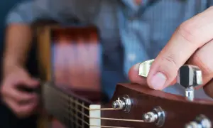 Dłoń z kostką do gitary kręci kluczem, by nastroić gitarę stroikiem.