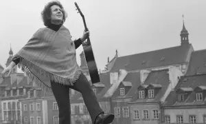 Tadeusz Woźniak, zegarmistrz światła, z gitarą na tle kamienic.