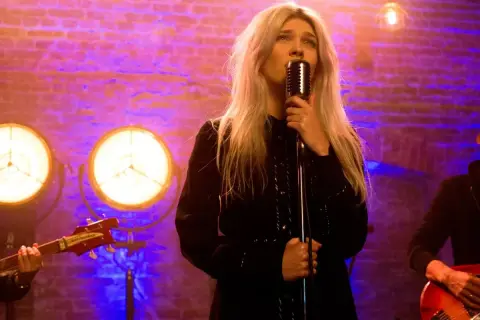 Daria Zawiałow śpiewa "Zielone Gramy" na koncercie. Wokalistka z blond włosami trzyma mikrofon, a w tle widać zespół i ceglaną ścianę.