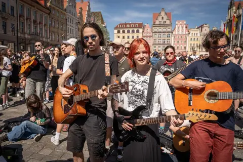Młodzi muzycy grają na gitarach na rynku, jakby to był wieczór, gdy się poznali.
