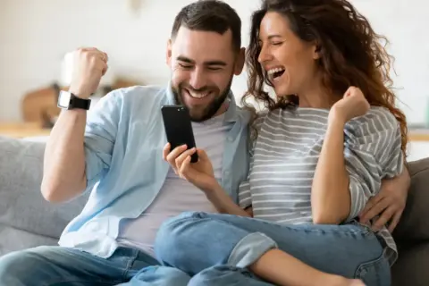 Para jak z liceum, zakochani, cieszą się z sukcesu, patrząc na telefon.