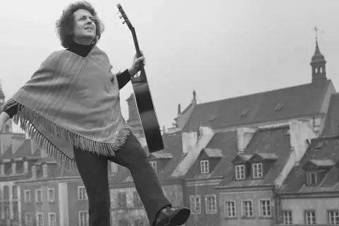 Tadeusz Woźniak, zegarmistrz światła, z gitarą na tle kamienic.