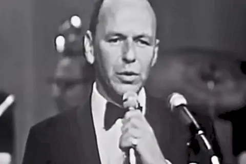 Frank Sinatra śpiewa "Fly Me to the Moon lyrics", ubrany w smoking.