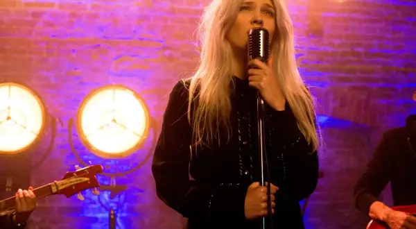 Daria Zawiałow śpiewa "Zielone Gramy" na koncercie. Wokalistka z blond włosami trzyma mikrofon, a w tle widać zespół i ceglaną ścianę.