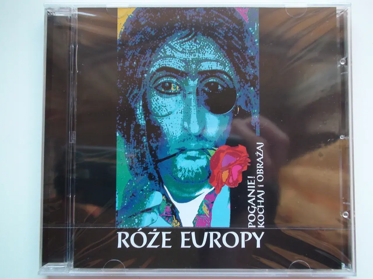 Okładka płyty "Róże Europy" z portretem w stylu pop-art, z różą w ustach i napisem "POGANIE! KOCHAJ i OBRAŻAJ".