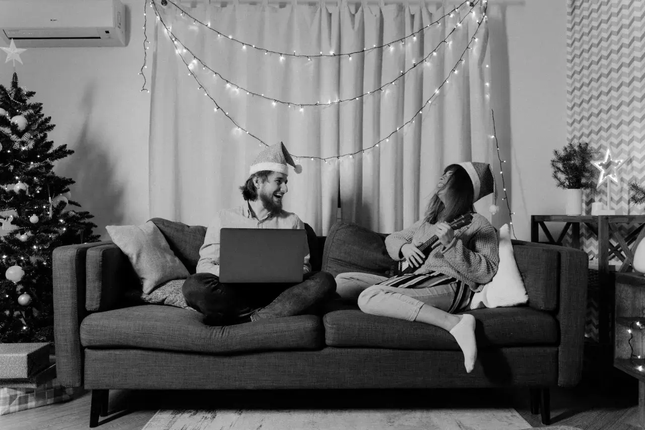 Wśród nocnej ciszy chwyty ukulele i śmiech przy laptopie. Para w czapkach Mikołaja cieszy się świąteczną atmosferą.