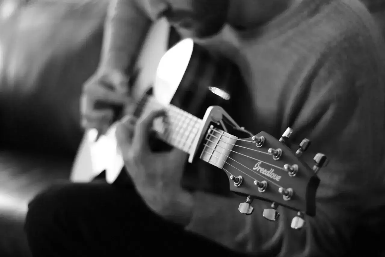 Czarno-białe ujęcie dłoni grającej na gitarze. Chcesz wiedzieć, jak zagrać na gitarze "Sto lat"? To proste, wystarczy ćwiczyć!