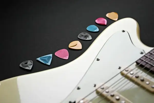 Różnokolorowe kostki do gitary elektrycznej leżą obok białej gitary. Wybierz odpowiednią, by zacząć naukę, jak nastroić gitarę elektryczną.