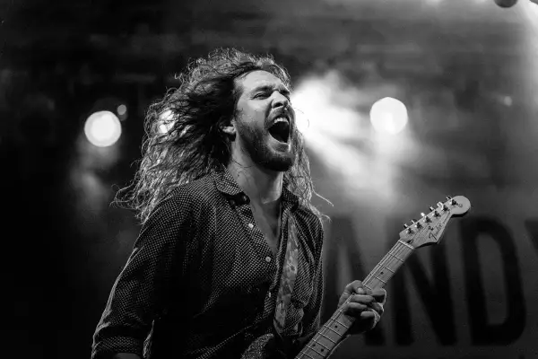 Charyzmatyczny gitarzysta z rozwianymi włosami śpiewa z pasją, grając na gitarze. Chcesz wiedzieć, jak zagrać Shallow na gitarze?