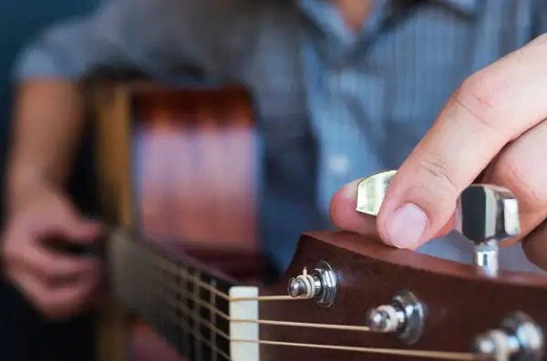 Dłoń z kostką do gitary kręci kluczem, by nastroić gitarę stroikiem.