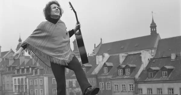 Tadeusz Woźniak, zegarmistrz światła, z gitarą na tle kamienic.