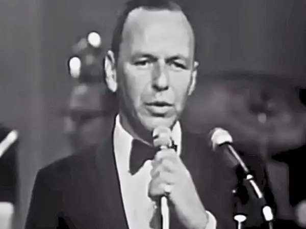 Frank Sinatra śpiewa "Fly Me to the Moon lyrics", ubrany w smoking.