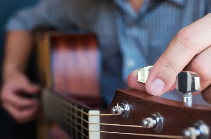 Dłoń z kostką do gitary kręci kluczem, by nastroić gitarę stroikiem.